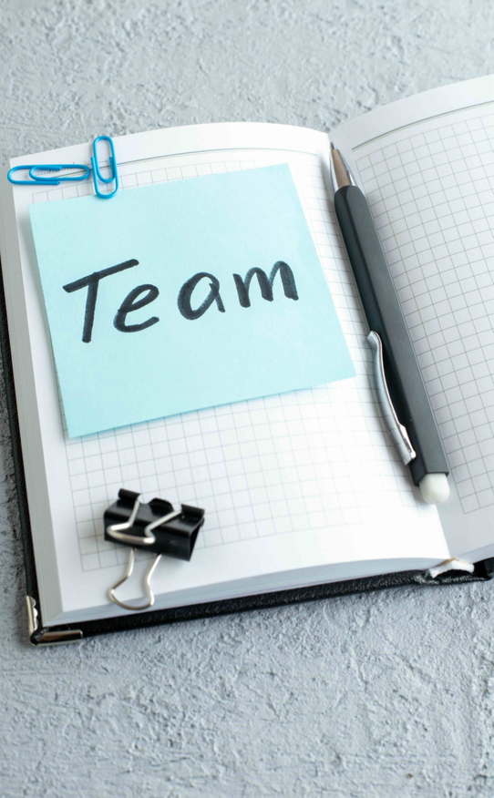 A photo of a note book open and a large blue postit note with the word Team