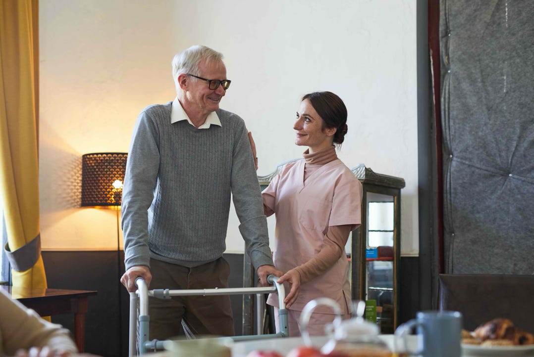 man walking with a zimmer frame being helped by a carer