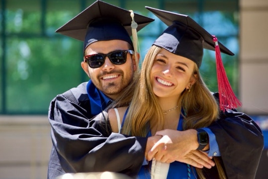 Photo of a man and woman both wearing graduation gowns and hats