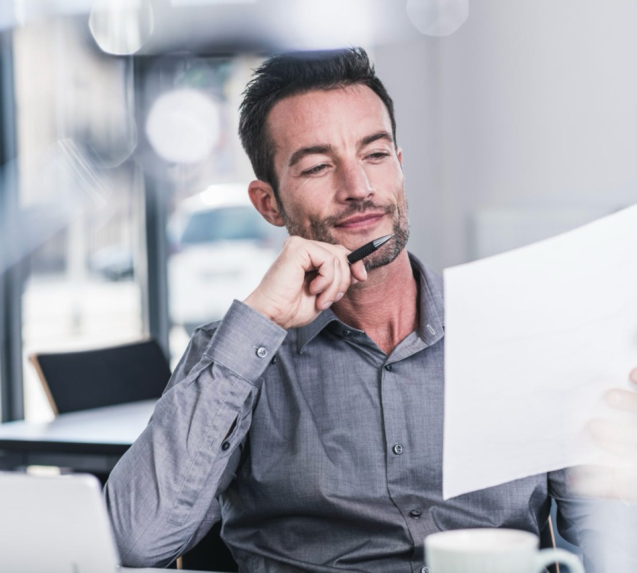 Man sat at desk with pen in hand and reading a sheet of paper