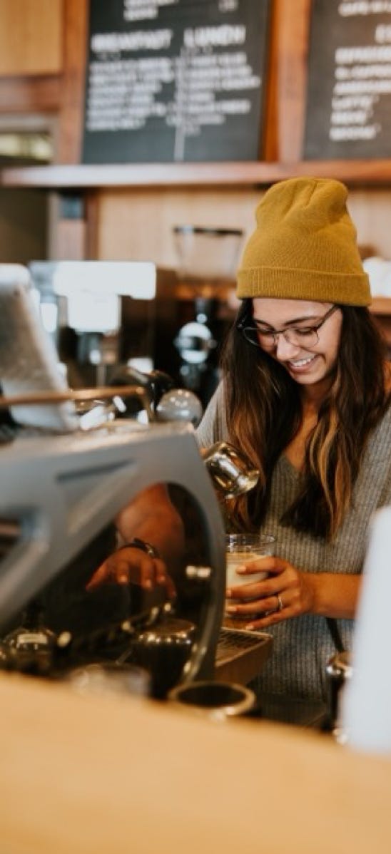 Young woman wearing a woollen hat working behind a counter making coffee