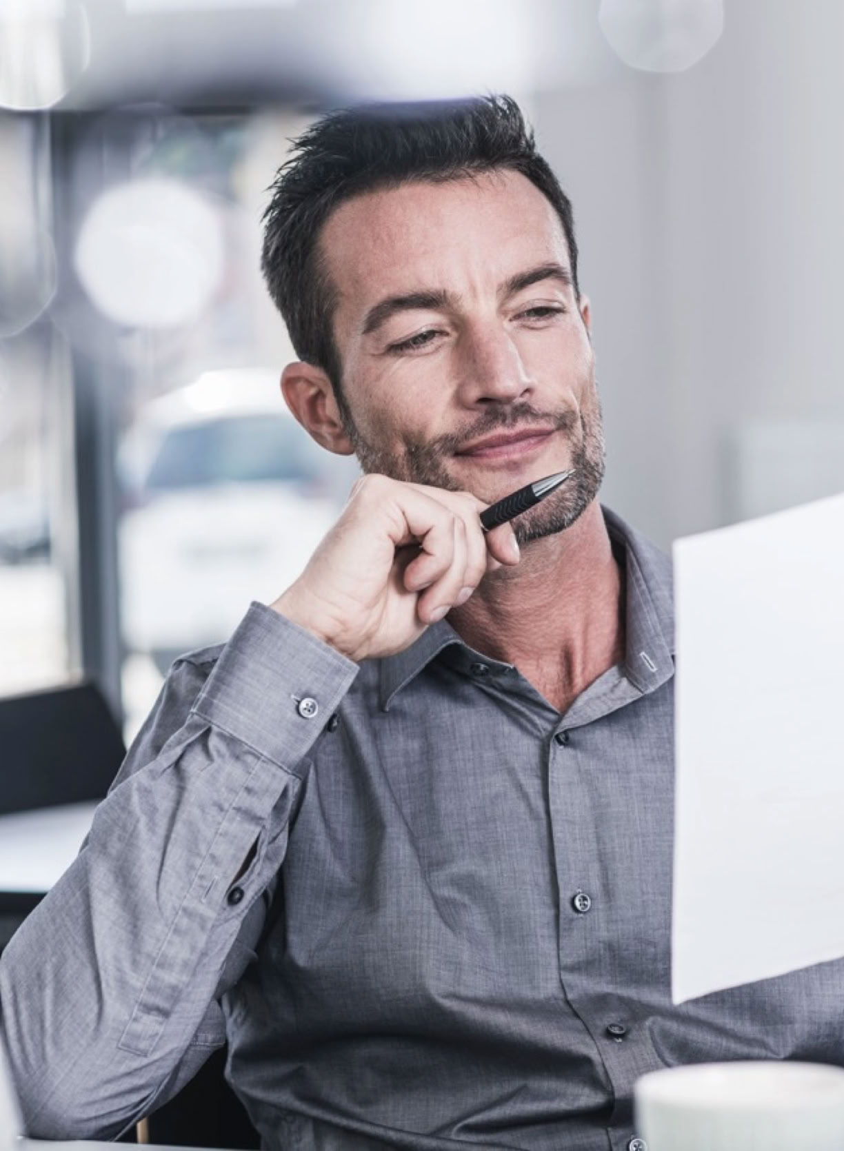 Man sat at desk with pen in hand and reading a sheet of paper